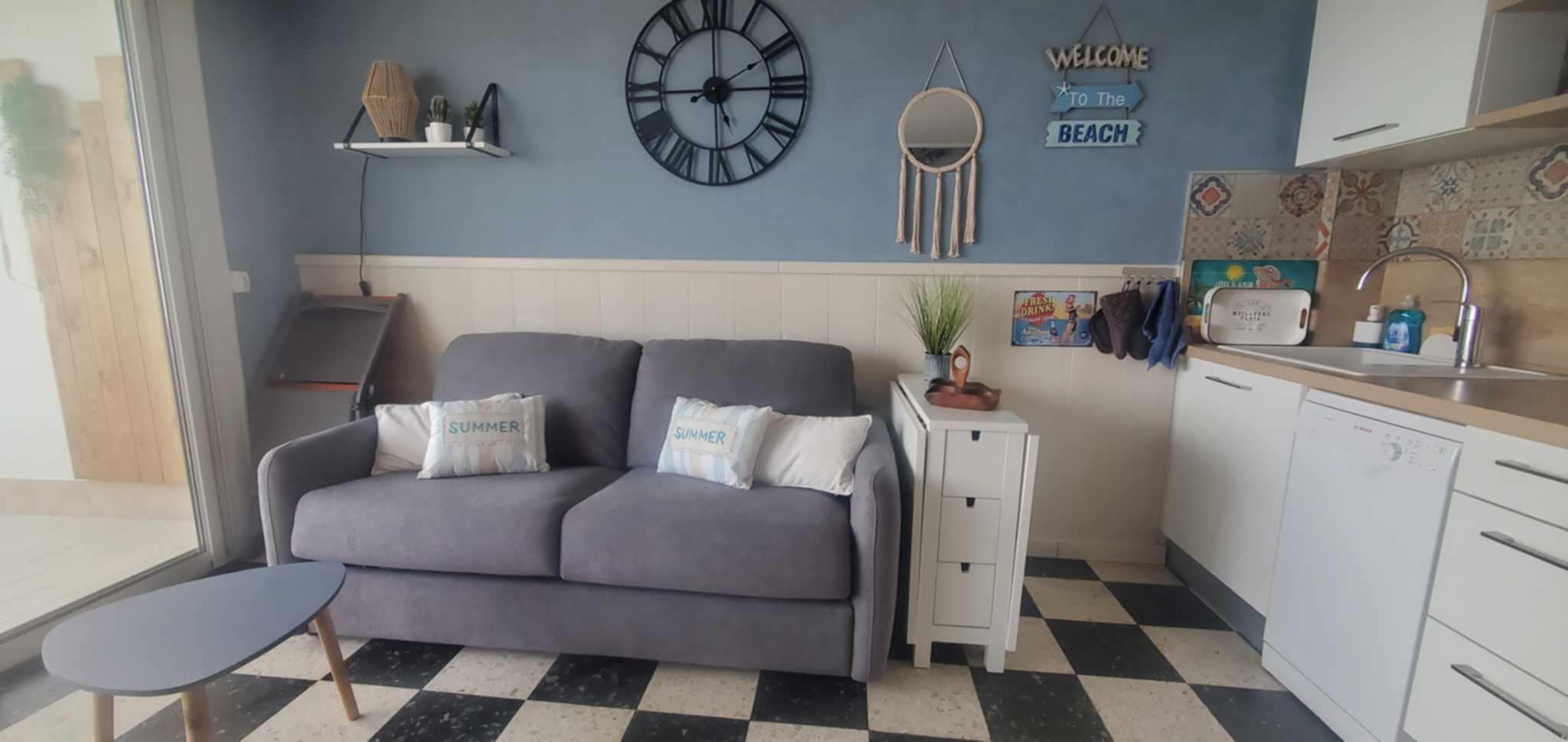 Salon confortable avec canapé gris et décoration estivale